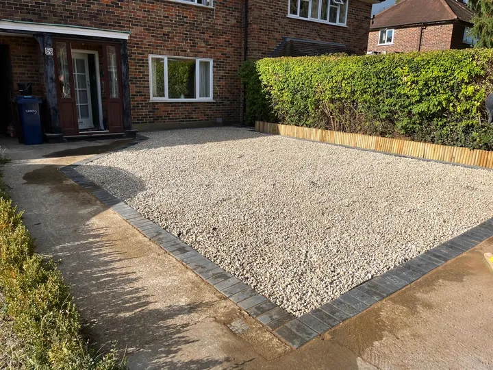 Freshly laid gravel driveway edged with a charcoal block-paved border in front of a red brick house