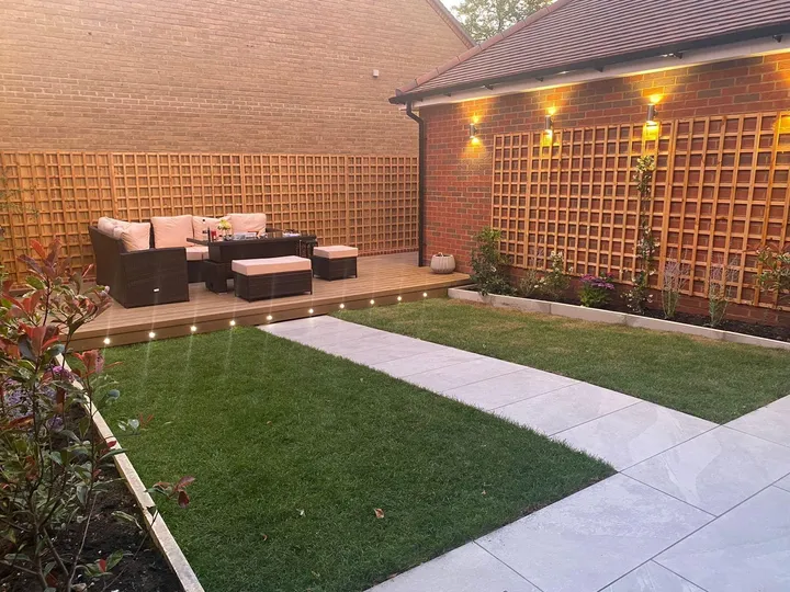Full garden transformation with decking, trellis, lawn and porcelain pathway at dusk with warm wall lighting