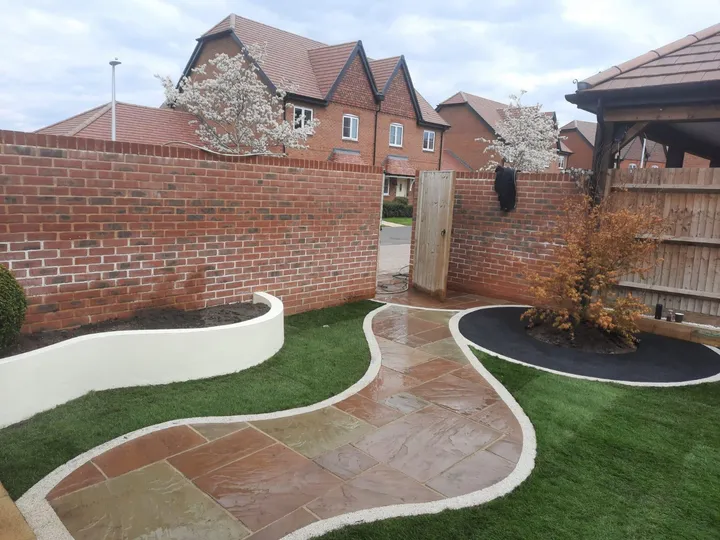 Curving Indian sandstone path sweeping between artificial lawn and a white rendered planter in a walled new-build garden
