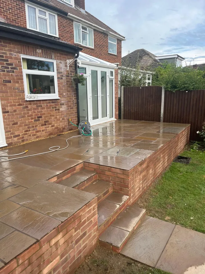Raised Indian sandstone patio held by red brick retaining walls with wide sandstone-capped steps down to the lawn