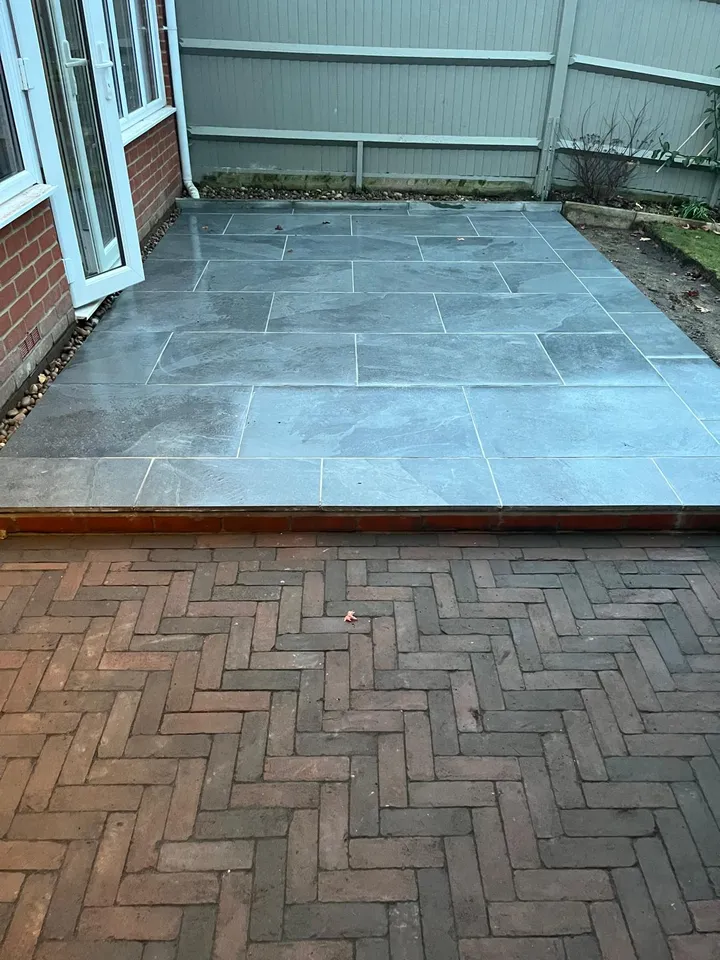 Grey porcelain patio meeting a herringbone block-paved path outside a conservatory
