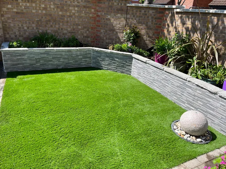 Slate-clad raised planting beds framing a flawless lawn with a stone sphere feature on a pebble bed